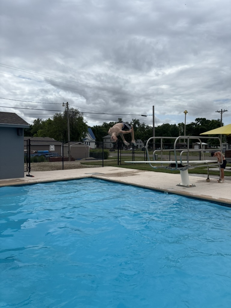 youth doing back flip off of diving board at municipal pool